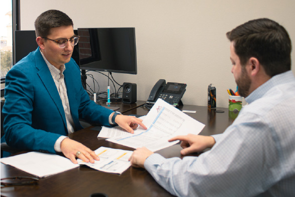 Two men talking over papers at a desk.